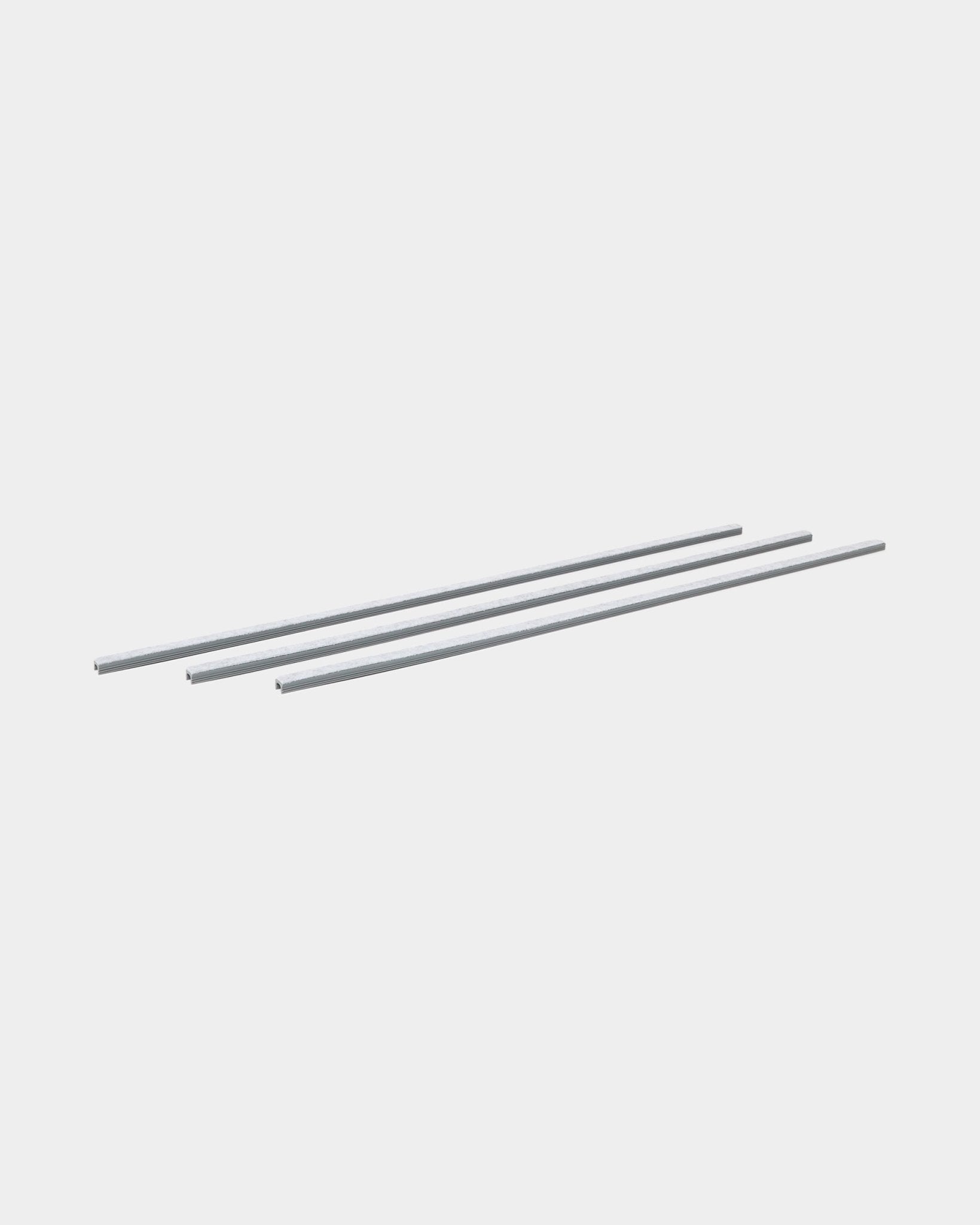 Drie grey Dupps Pop-on Cable Covers (3 stuks) van WoodUpp liggen parallel naast elkaar en zijn ontworpen om kabels te organiseren met Akupanel akoestische houten panelen.